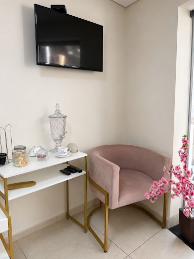 Cantinho de espera com poltrona rosa, aparador branco com detalhes dourados e flores